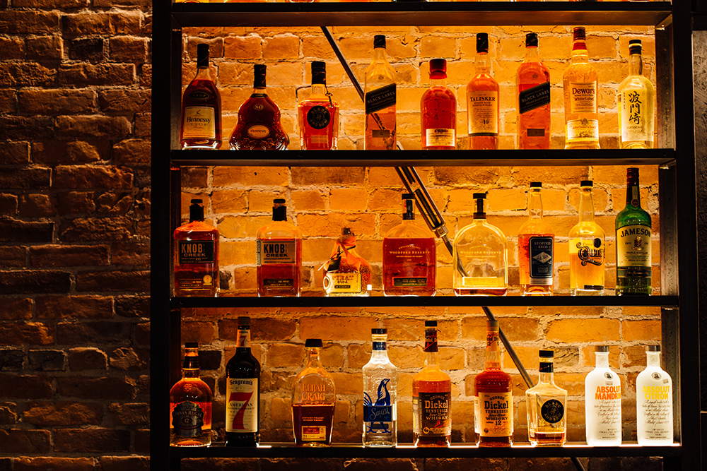 Image of part of the Imogene's whiskey wall, warmly lit with a restored brick wall backdrop.